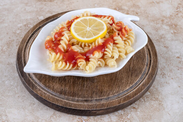 Wooden board with a platter of lemon-topped pasta on marble background