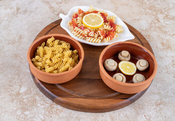 Two portions of pasta with a bowl of mushrooms on marble background