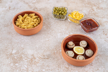 Bowl of cooked paste and portions of various toppings on marble background