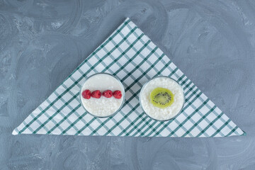 Bowls of rice pudding garnished with raspberries and kiwi slice on a tablecloth on marble background