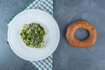 Portion of bean pulses cooked with eggs, next to a bagel on marble background