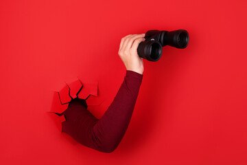 binoculars in hand over red background