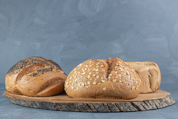 Wooden board under three loaves of bread on marble background