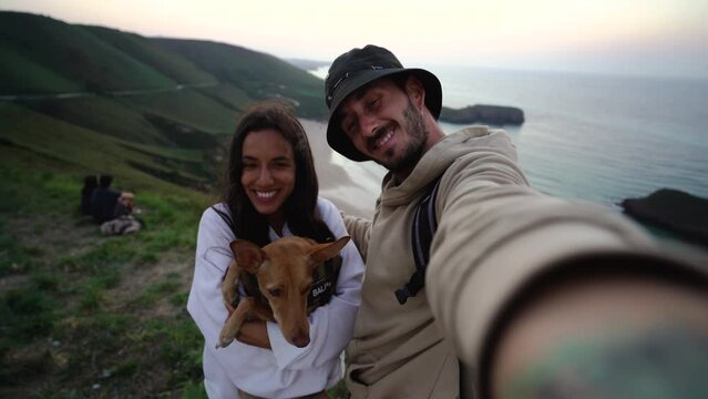 couple of lovers taking a selfie from a stunning ocean cliff with their cute little dog for a memory from holiday