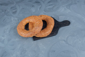 Two sesame covered bagels on a black wooden board on marble background