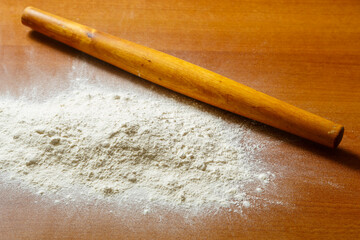 Flour is scattered on a wooden table and a rolling pin for dough lies.