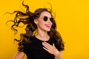 Photo of impressed pretty young woman wear black outfit dark eyeglasses air blowing looking empty space isolated yellow color background