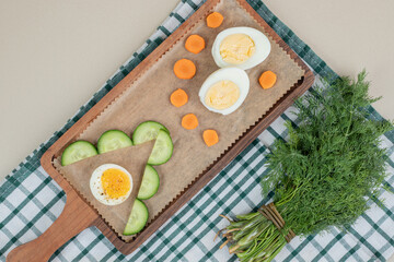 A wooden cutting board with sliced cucumber and boiled egg