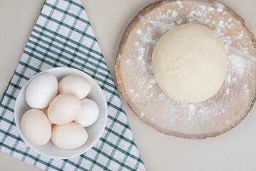 Dough with three chicken fresh white eggs on wooden cutting board