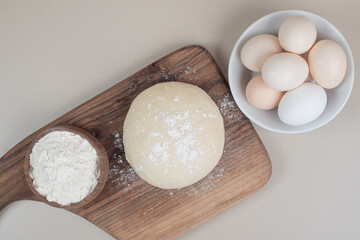 Dough with three chicken fresh white eggs on wooden cutting board
