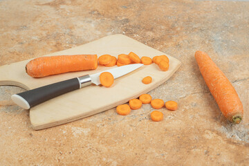 A wooden cutting board with sliced carrot and knife
