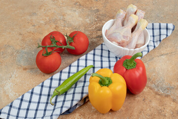 Peppers with tomatoes and raw chicken legs on tablecloth
