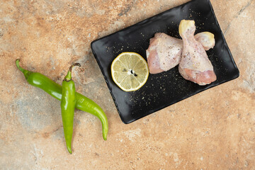 A dark plate of uncooked chicken legs with sliced lemon