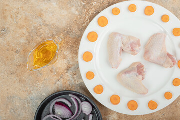 Uncooked chicken leg with sliced carrot on white plate