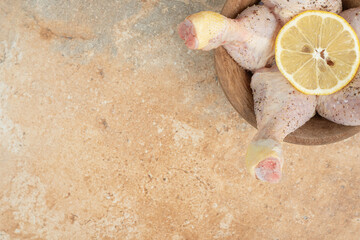 Raw chicken legs with sliced lemon on marble background