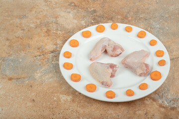 Uncooked chicken leg with sliced carrot on white plate