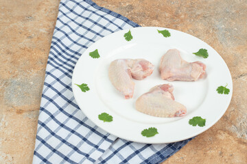 Uncooked chicken leg with greens on white plate
