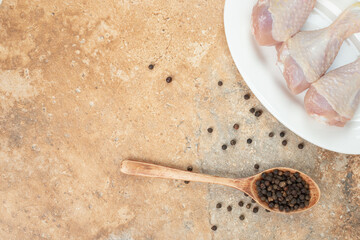 A white plate with uncooked chicken leg with wooden spoon of pepper