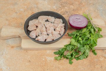 Uncooked chicken legs in dark pan with sliced onion