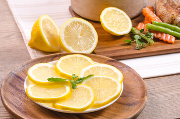 Close-up of fresh organic lemon with peppermint in the wooden plate on wood table.