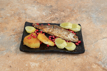 Herring with fried potatoes and pickles on black plate