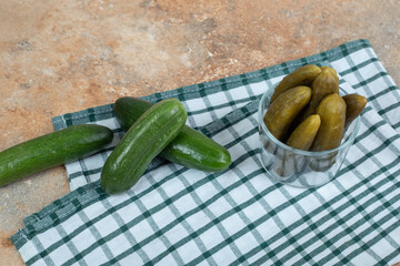 Bowl of pickles and fresh cucumbers on tablecloth