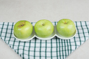 Whole green apples on white plates with striped tablecloth