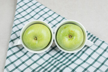 Whole green apples in white cups with tablecloth