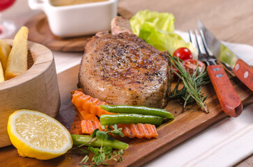The delicious grilled ribeye beef steak on the wooden cutting board with french fries and fresh vegetables salad.