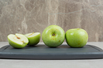 Whole and half cut green apples on dark plate