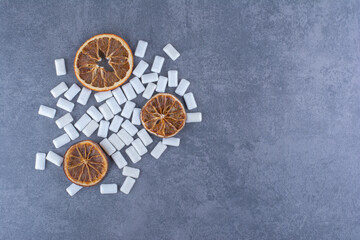 Messy bundle of gum tablets in the middle of dried orange slices on marble background