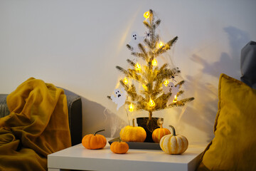 Halloween house decoration. Christmas tree with cobweb lights and ghosts. Decorative pumpkins in the interior.