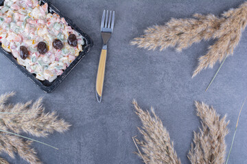 Oliver salad with olive garnish next to decorative dried needlgrass stalks on marble background