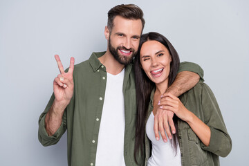Portrait of handsome beautiful trendy cheerful couple cuddling showing v-sign isolated over grey...