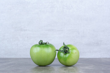 Two green tomatoes on marble background