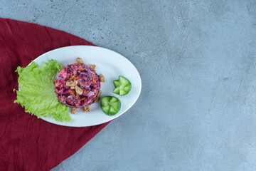 Cucumber slices and lettuce leaf next to beetroot and walnut salad on marble background