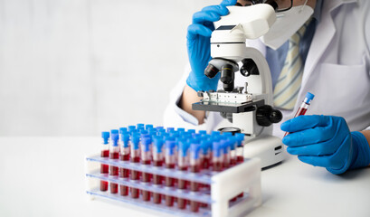 Doctor hand taking a blood sample tube from a rack with machines of analysis in the lab background, Technician holding blood tube test in the research laboratory.