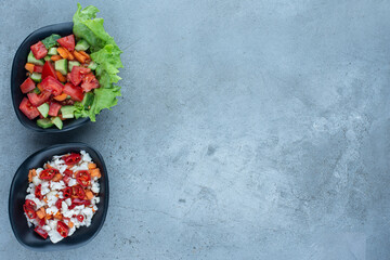 Two bowls of shepherd's salad next to a bowl of pepper and cauliflower salad on marble background