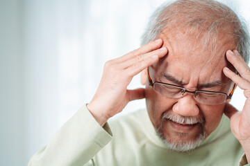 Closeup of Asian Senior elderly old man feel headache suffering and migraine in living room at home. Stressed mature male hurt mental health care and insurance concept.