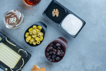 Bread, cheese, black and green olives, chocolate, oatmeal and a cup of tea in a breakfast set on marble background