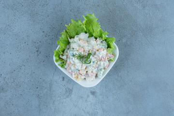 Small bowl of olivier salad with a lettuce leaf on marble background