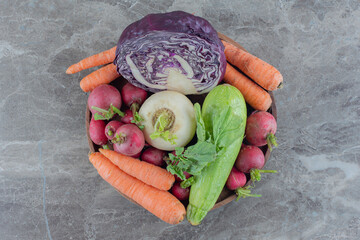 Wooden bowl stocked with red and white turnips, carrots, squash and red cabbage on marble background