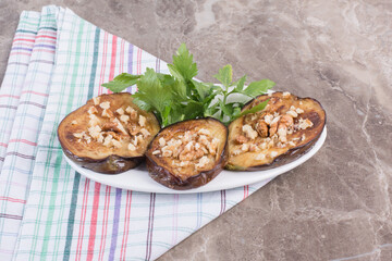 Platter of friend indian eggplant slices topped with parsley leaves and garlic bits on marble background