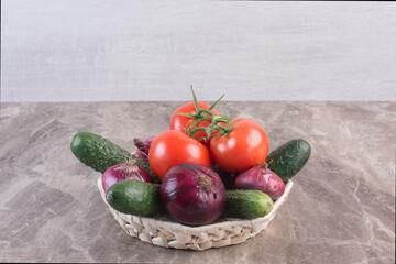 Basket filled with cucumber, red onion and tomato on marble background