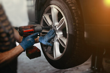 Fototapeta premium Seasonal replacement of car tires, a man unscrews the wheel with a screwdriver.