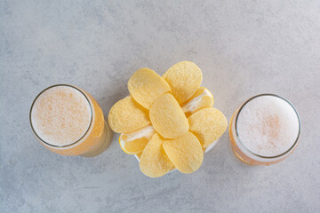 Two glasses of beer with potato chips on gray background