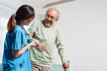 Asian senior elderly man patient doing physical therapy with caregiver. woman nurse helping get up from wheelchair for practice walking with walker at home, practice walk slowly at nursing home care.