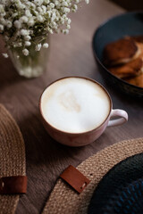 Closeup of the cup of coffee with white foam and some pancakes on the wooden table