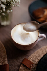 Closeup of the cup of coffee with white foam and some pancakes on the wooden table