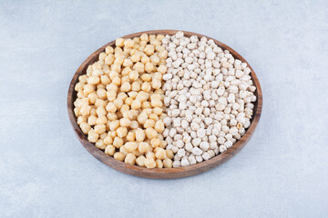 Large wooden tray stocked with piles of cooked and raw chickpeas on marble background